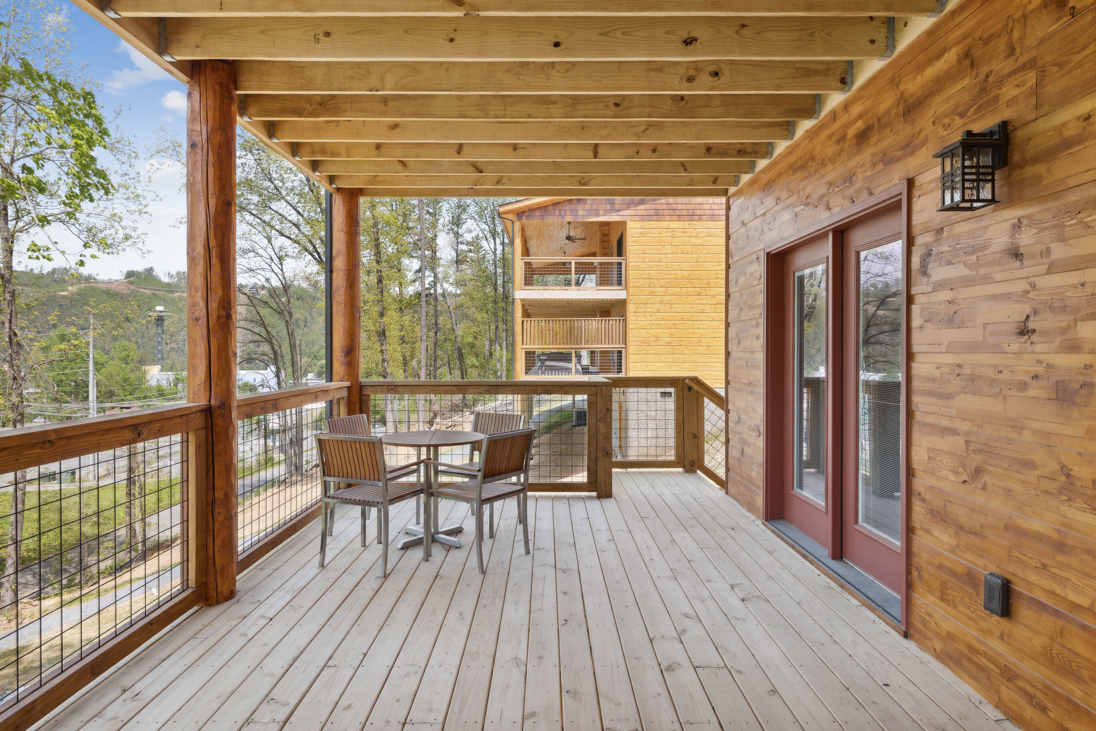 A wooden deck with a table and chairs, overlooking a forested area.