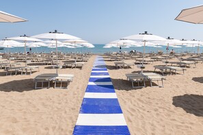 A beach with rows of sun loungers and umbrellas, a blue-striped pathway leading to the sea. - Seven Air Apartment (Lido di Jesolo)