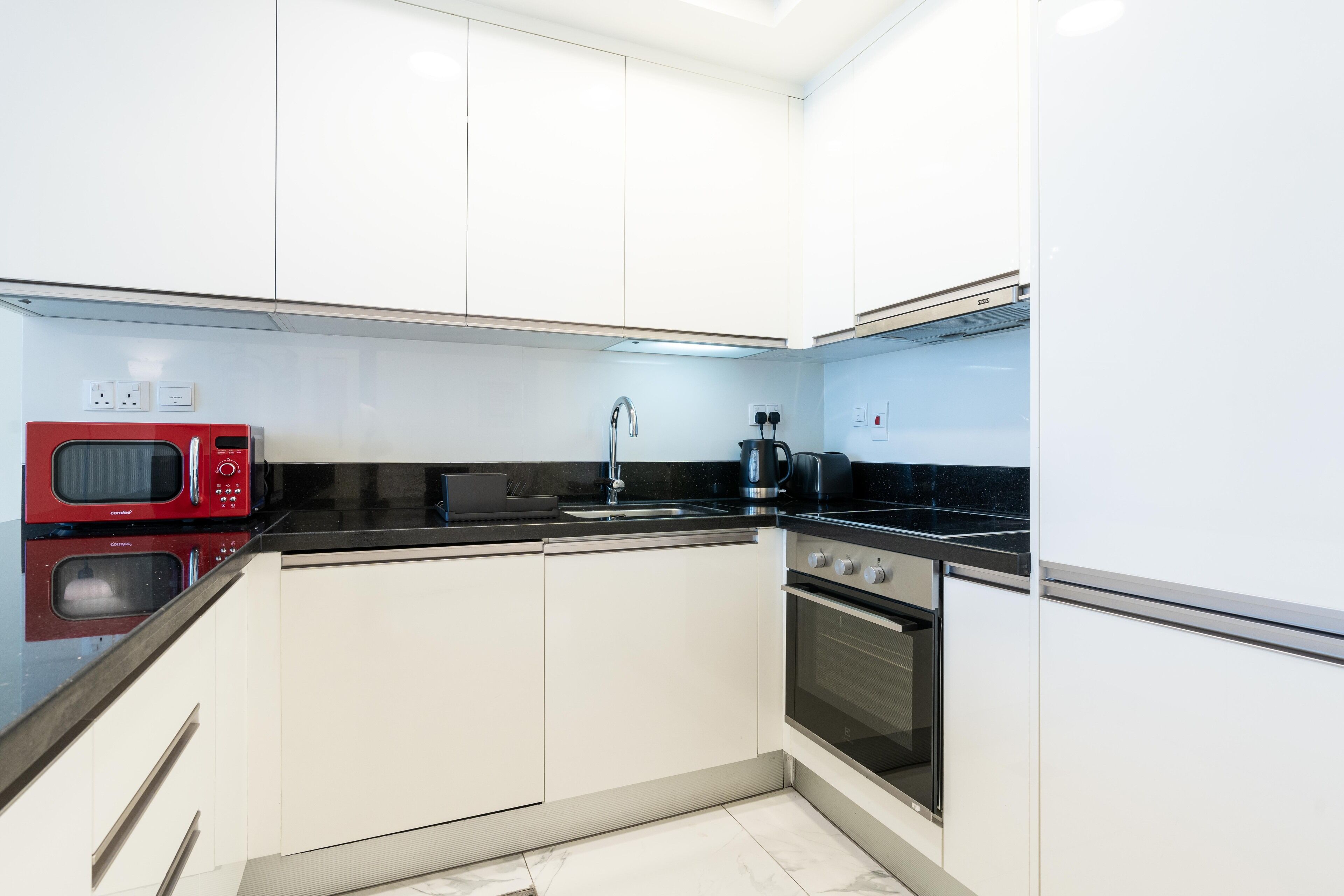 Una cocina moderna con armarios blancos, un microondas rojo, una estufa negra y un fregadero de acero inoxidable.