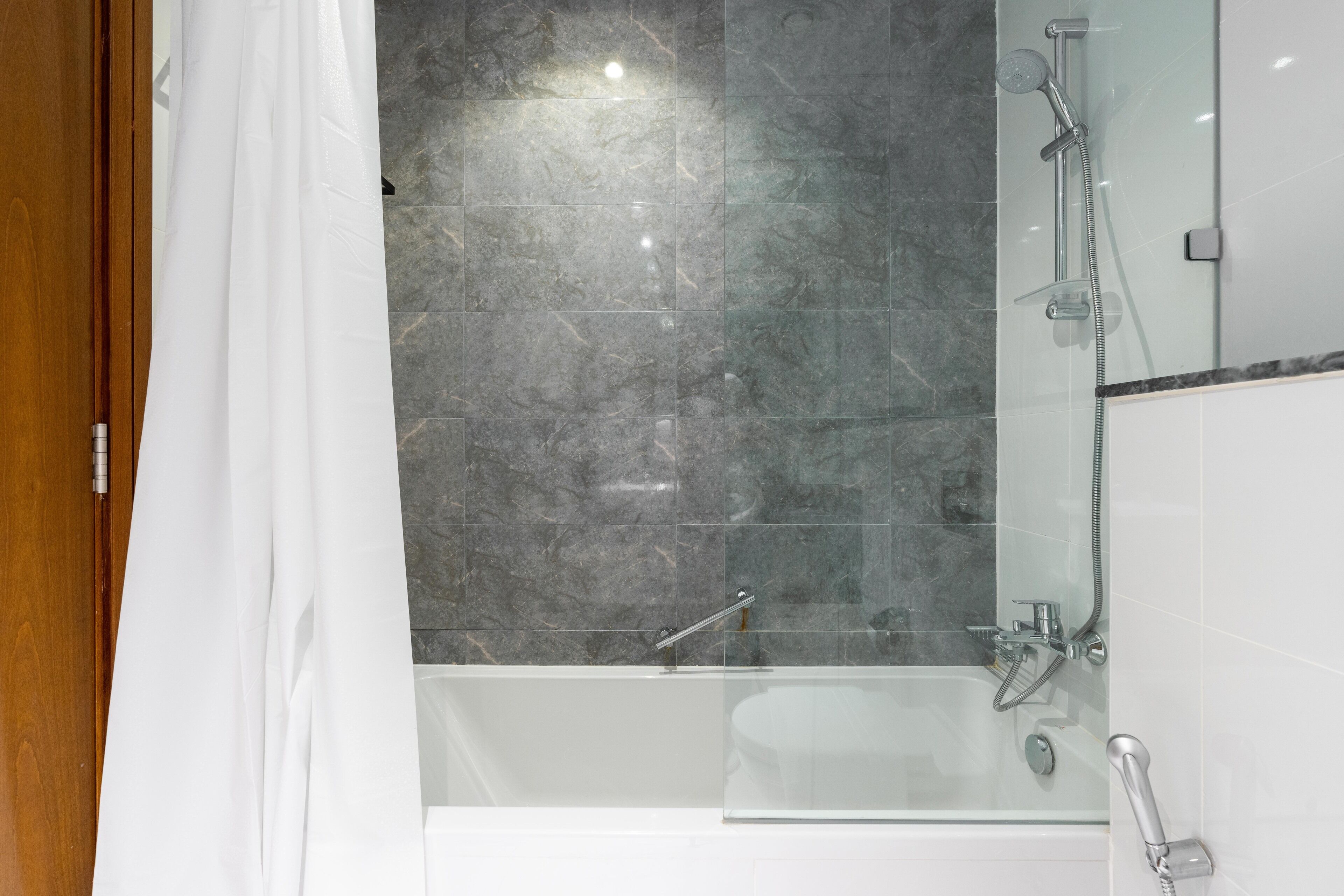A modern bathroom with a glass-enclosed shower, a white bathtub, and a marble-tiled wall.