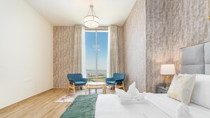 A hotel room with a large bed, two chairs, a small table, a nightstand with a lamp, and a view of the city through a large window. - Lux BnB I Amna Tower I Panaromic Views (Dubai)