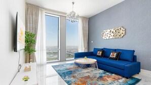 A modern living room with a blue sofa, a round coffee table, and a city view through large windows. - Lux BnB I Amna Tower I Panaromic Views (Dubai)