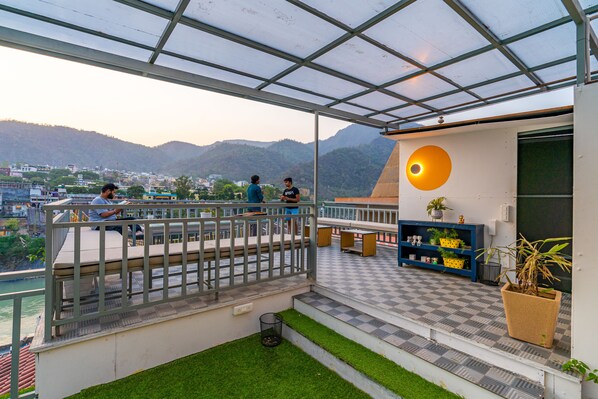 A rooftop terrace with a view of the city and mountains, a checkered floor, and a blue shelving unit with plants. - Madpackers Rishikesh (Yamkeshwar)