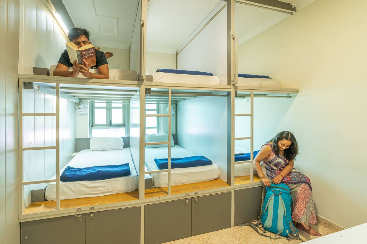 A bunk bed room with a window, a suitcase, and a person reading a book.
