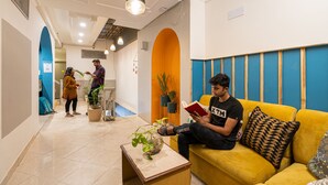 A modern hotel lobby with a yellow sofa, a coffee table, and potted plants. - Madpackers Rishikesh (Yamkeshwar)