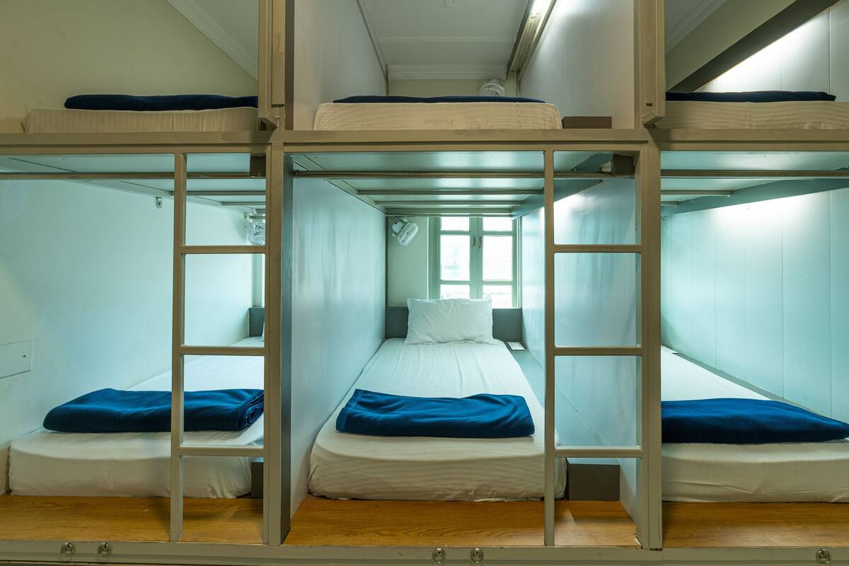 A bunk bed room with a central bed flanked by two single beds, each with a blue blanket.