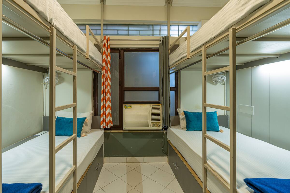 A dormitory room with bunk beds, a window, and a fan.
