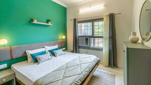 A bedroom with a bed, nightstands, a window with curtains, a dresser, and a mirror. - Madpackers Rishikesh (Yamkeshwar)