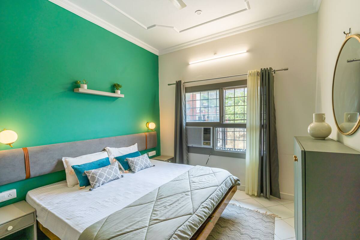 A bedroom with a bed, nightstands, a window with curtains, a dresser, and a mirror.