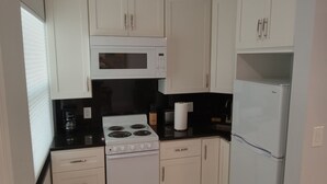 Een kleine keuken met witte kastjes, een witte kookplaat, een magnetron en een koelkast.