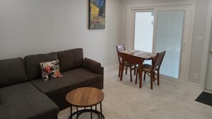 Een woonkamer met een hoekbank, een kleine houten tafel, en een eethoek met een houten tafel en stoelen.