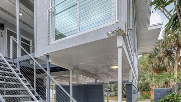 Een modern gebouw met een overdekt terras, een metalen trap en een pad van bakstenen.