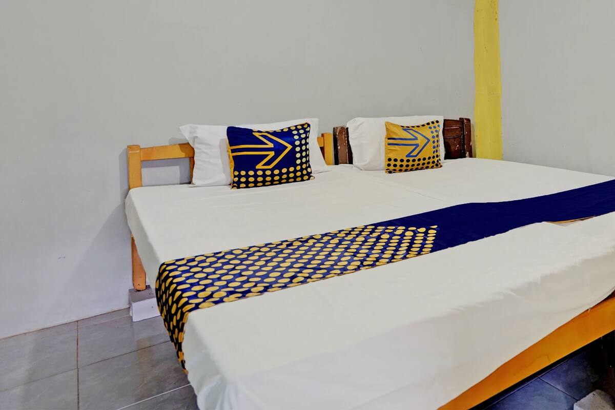 A bed with a white and blue patterned bedspread, two pillows with blue and yellow designs, and a wooden headboard.