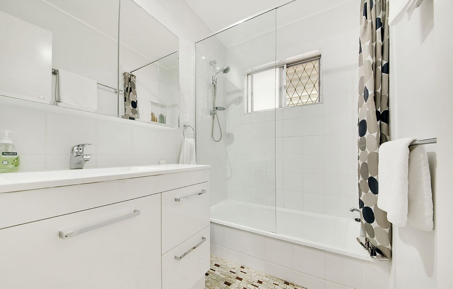 Une salle de bain moderne avec un meuble-lavabo blanc, une cabine de douche en verre et un rideau de douche à motifs.