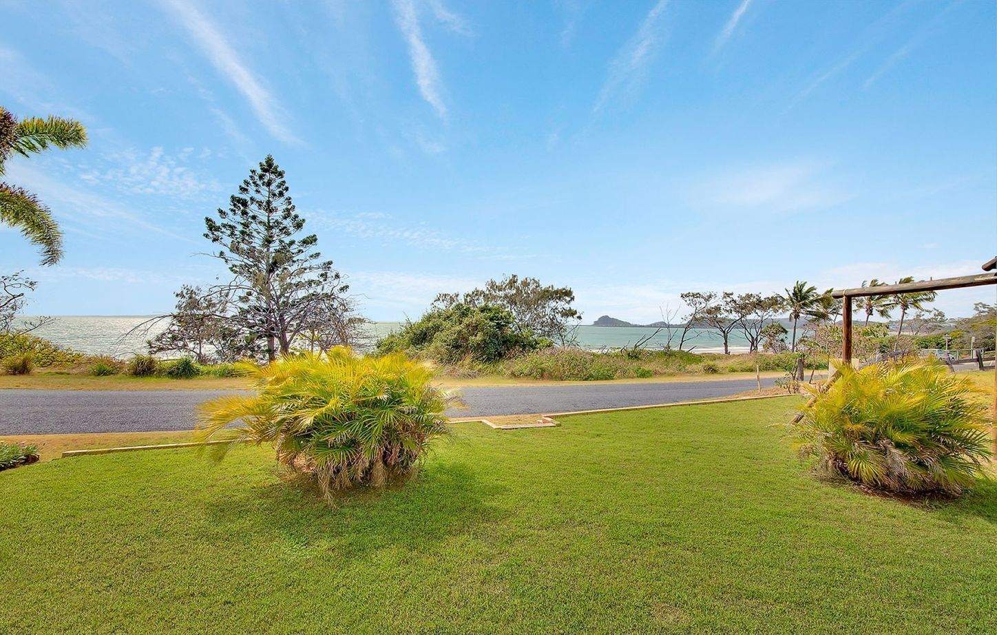 A grassy area with a road, trees, and a clear sky.
