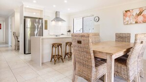 Una cocina moderna con un refrigerador de acero inoxidable, una isla central con taburetes y una mesa de comedor con sillas de mimbre.