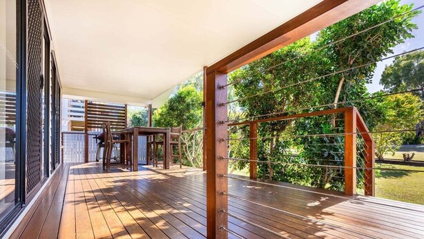 Una terraza de madera al aire libre con vistas a vegetación exuberante y un cielo despejado.