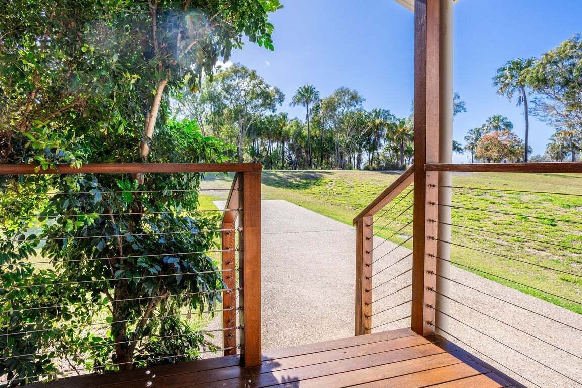 A wooden staircase leading to a covered outdoor area with a view of a grassy field and trees.