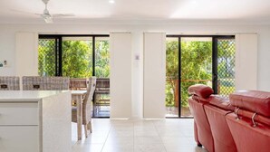 Un espacio habitable amplio con un sofá rojo, una mesa de comedor con sillas de mimbre y vistas a un jardín a través de grandes puertas correderas de cristal.