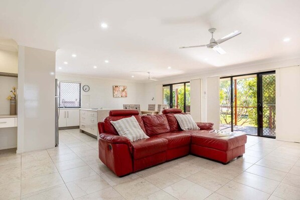 A spacious living area with a red leather sofa, a ceiling fan, and a large sliding glass door to the outdoors.