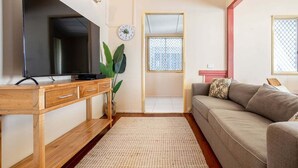 A living room with a flat-screen TV on a wooden stand, a sofa, a coffee table, and a large window with a view. - The Normanby - For the traveller on a budget (Yeppoon)