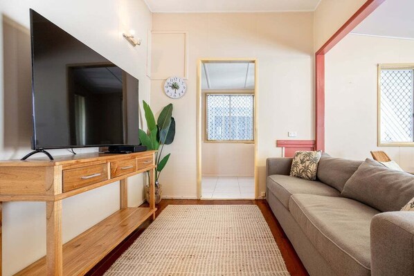 A living room with a flat-screen TV on a wooden stand, a sofa, a coffee table, and a large window with a view. - The Normanby - For the traveller on a budget (Yeppoon)