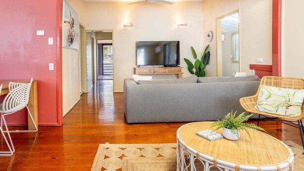 A living room with a grey sofa, a television, a ceiling fan, and a wicker coffee table. - The Normanby - For the traveller on a budget (Yeppoon)