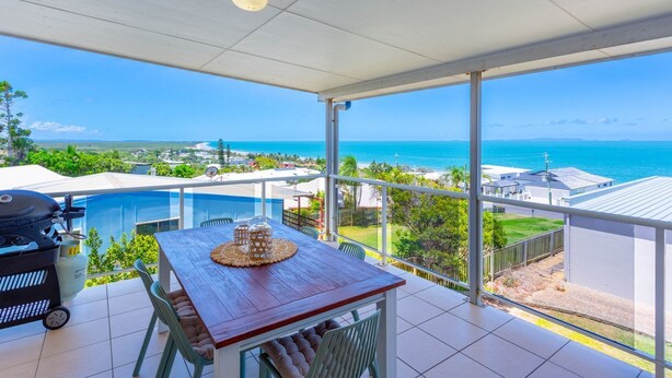 A balcony with a wooden table, chairs, and a view of the ocean. - Catalina Island Views - What an understatement! (Yeppoon)