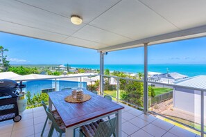 A balcony with a wooden table, chairs, and a view of the ocean. - Catalina Island Views - What an understatement! (Yeppoon)