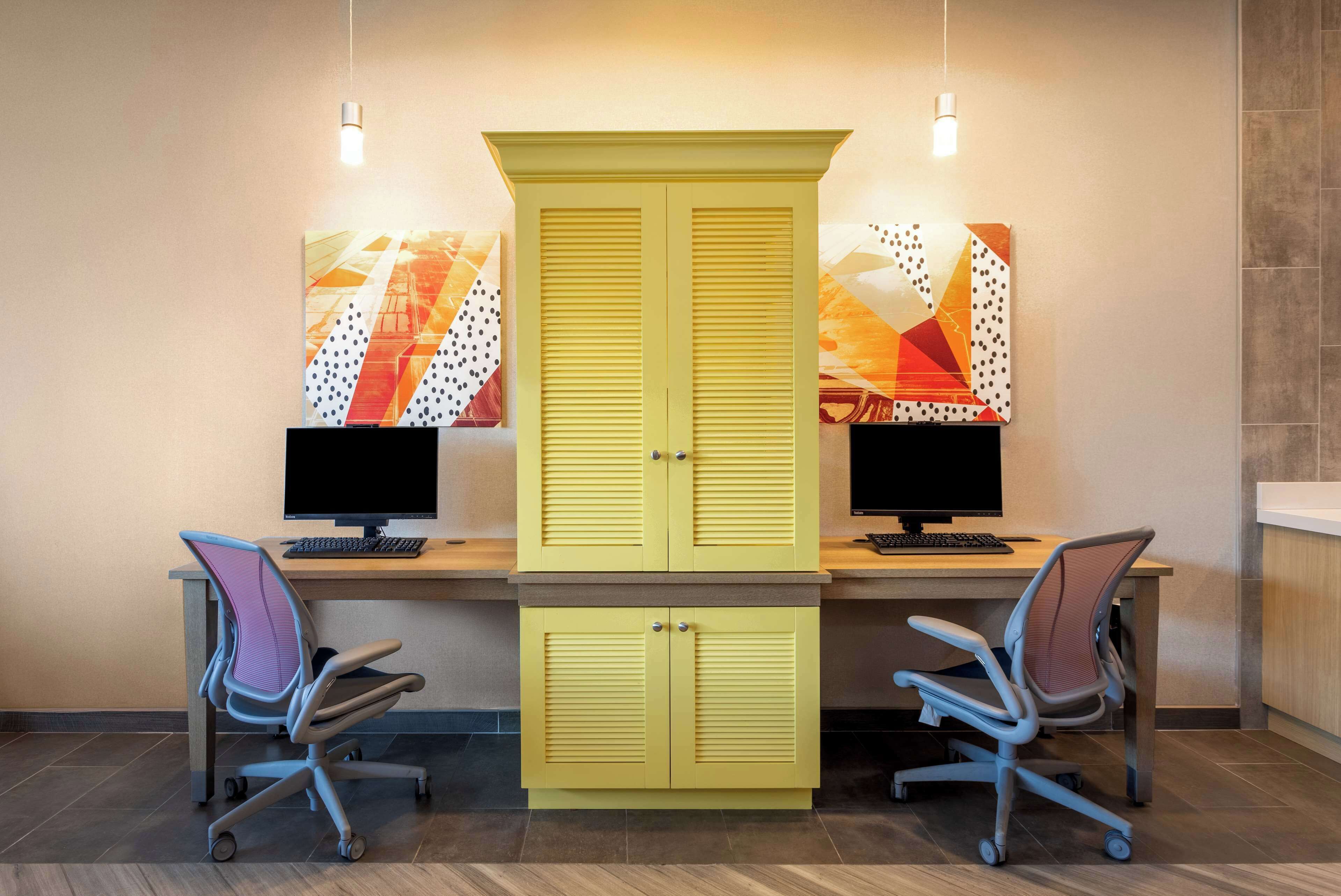 Un espace de travail comprenant deux bureaux, chacun équipé d’un ordinateur et d’une chaise ergonomique. Un grand meuble jaune se trouve au centre de la pièce.