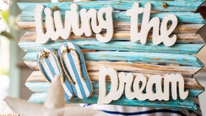 Ein dekoratives Schild mit der Aufschrift "Living the Dream" und einem Paar gestreifter Flip-Flops.