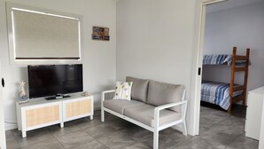 Ein kleiner, ordentlich eingerichteter Raum mit Fernseher, einer Couch, einem kleinen Schrank und einem Etagenbett.