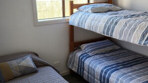 Ein Schlafsaalzimmer mit zwei Etagenbetten, einem Fenster mit Blick auf einen Zaun und einer schlichten Wand.