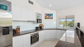 A modern kitchen with white cabinets, a granite countertop, a built-in oven, and a window with blinds.
