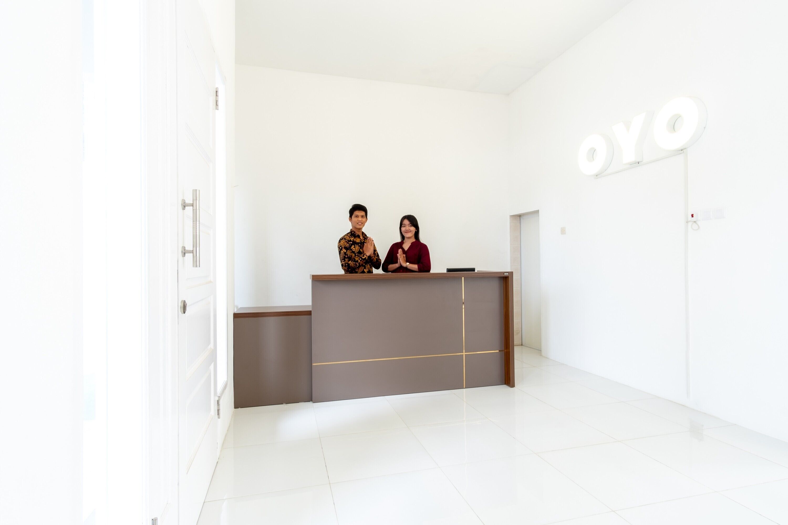 Un comptoir d’accueil avec une enseigne indiquant « OYO », situé dans un intérieur moderne et lumineux, avec des murs blancs et un sol carrelé.