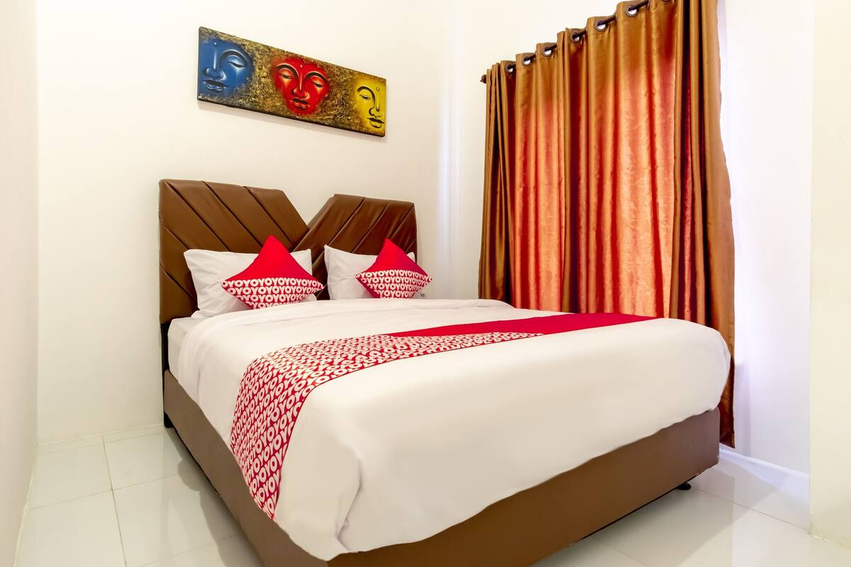 Una cama bien hecha con una colcha estampada y almohadones, un cabecero de diseño único y una obra de arte colgada en la pared.