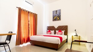 Habitación de hotel con cama, escritorio, silla, mesita de noche y un cuadro en la pared.