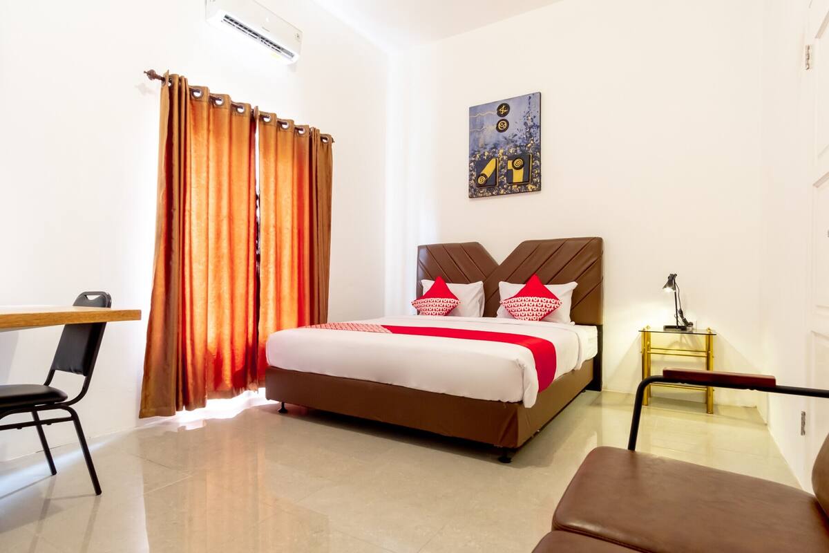 Habitación de hotel con cama, escritorio, silla, mesita de noche y un cuadro en la pared.