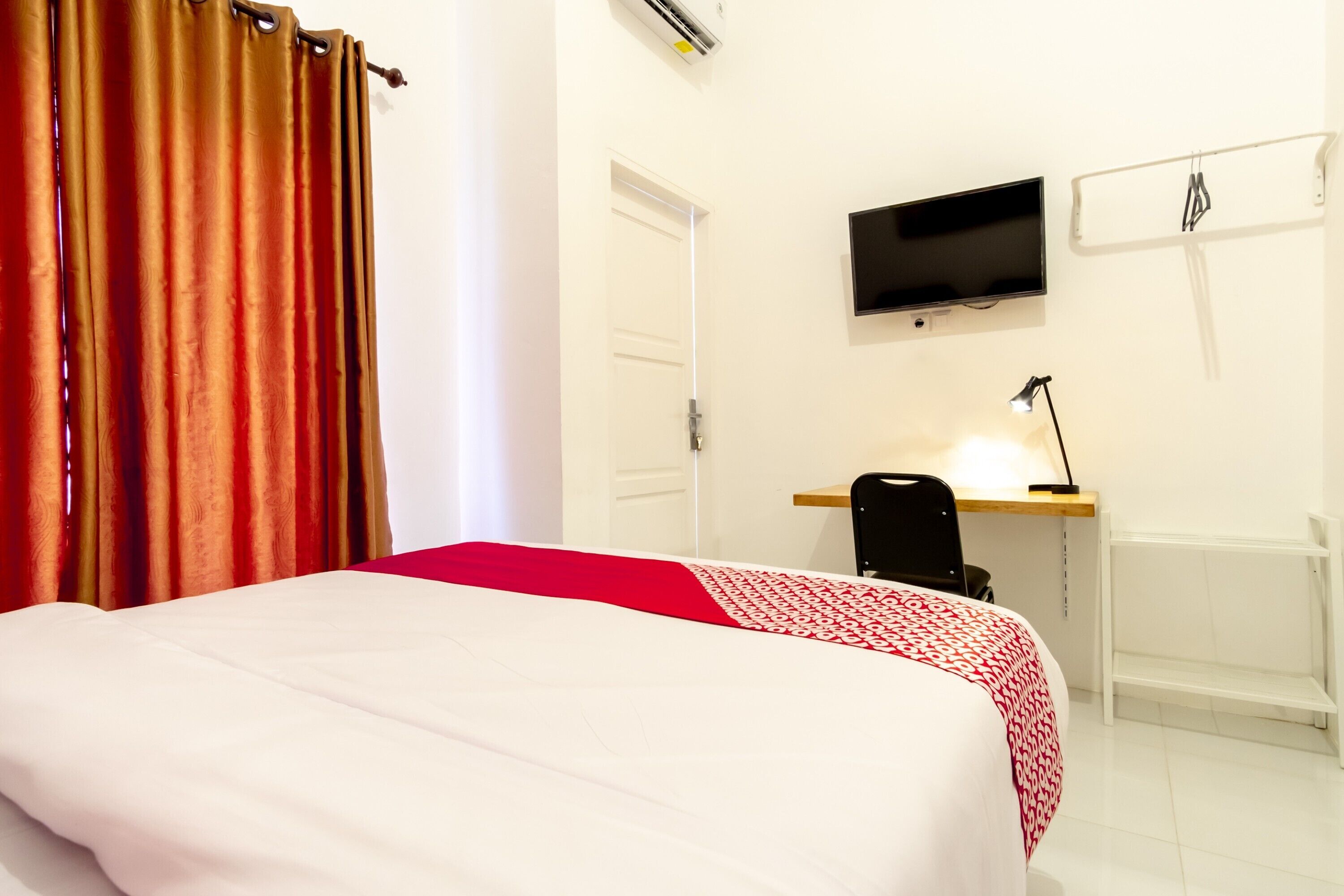 A hotel room with a bed, a desk, a chair, a TV, and a wardrobe.