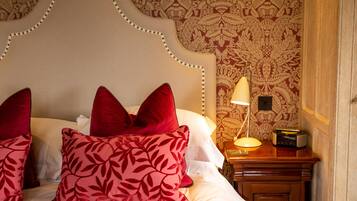 A neatly made bed with red and pink patterned pillows, a classic headboard, and a bedside table with a lamp and radio.