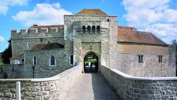 A stone building with a central archway, a paved pathway leading to it, and a stone wall on one side.