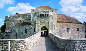 A stone building with a central archway, a paved pathway leading to it, and a stone wall on one side.