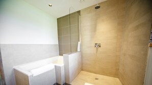 Une salle de bain moderne équipée d’une baignoire, d’une douche et d’un espace de douche séparé par des parois en verre.