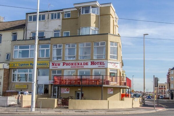 A multi-story hotel with a prominent sign for the New Promenade Hotel, featuring a balcony with red railings. - New Promenade hotel (Blackpool)