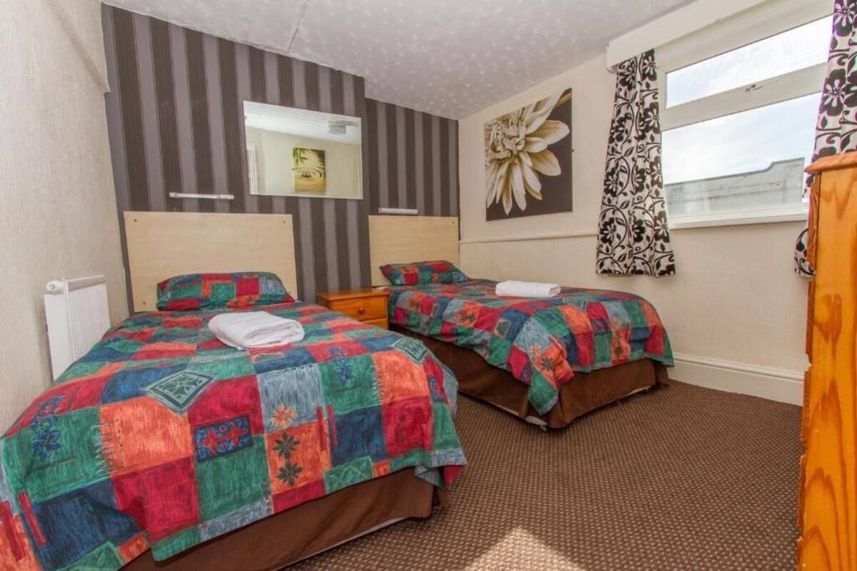 A hotel room with two beds, striped wallpaper, a large floral artwork, and a window with patterned curtains.