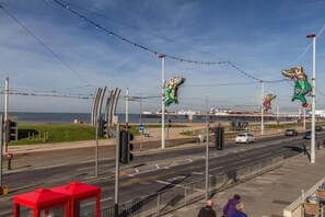 A coastal road with a pedestrian walkway, street lamps, and a red bus stop. - New Promenade hotel (Blackpool)