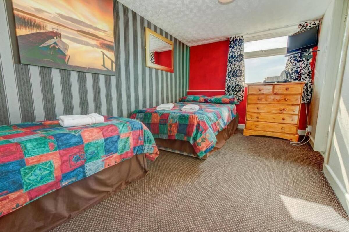 A hotel room with two beds, a dresser, a TV, and a large window.