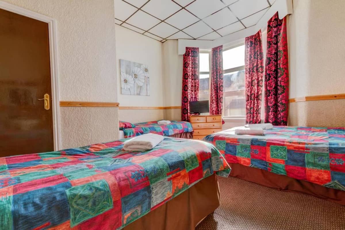 A room with two beds, a wooden dresser, a television, and a window with curtains.