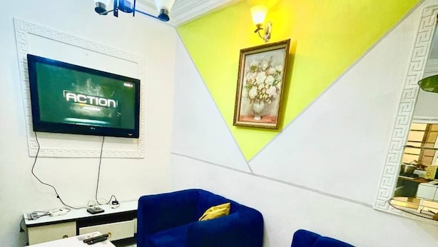 A living room with a TV, two blue sofas, a white coffee table, and a yellow wall. - 1 Bed Studio Sleeps 2 - Wifi, Balcony, Parking (Douala)
