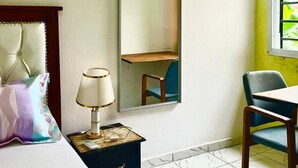 A hotel room with a bed, a bedside table with a lamp, a chair, a mirror, and a window with a view of greenery. - 1 Bed Studio Sleeps 2 - Wifi, Balcony, Parking (Douala)